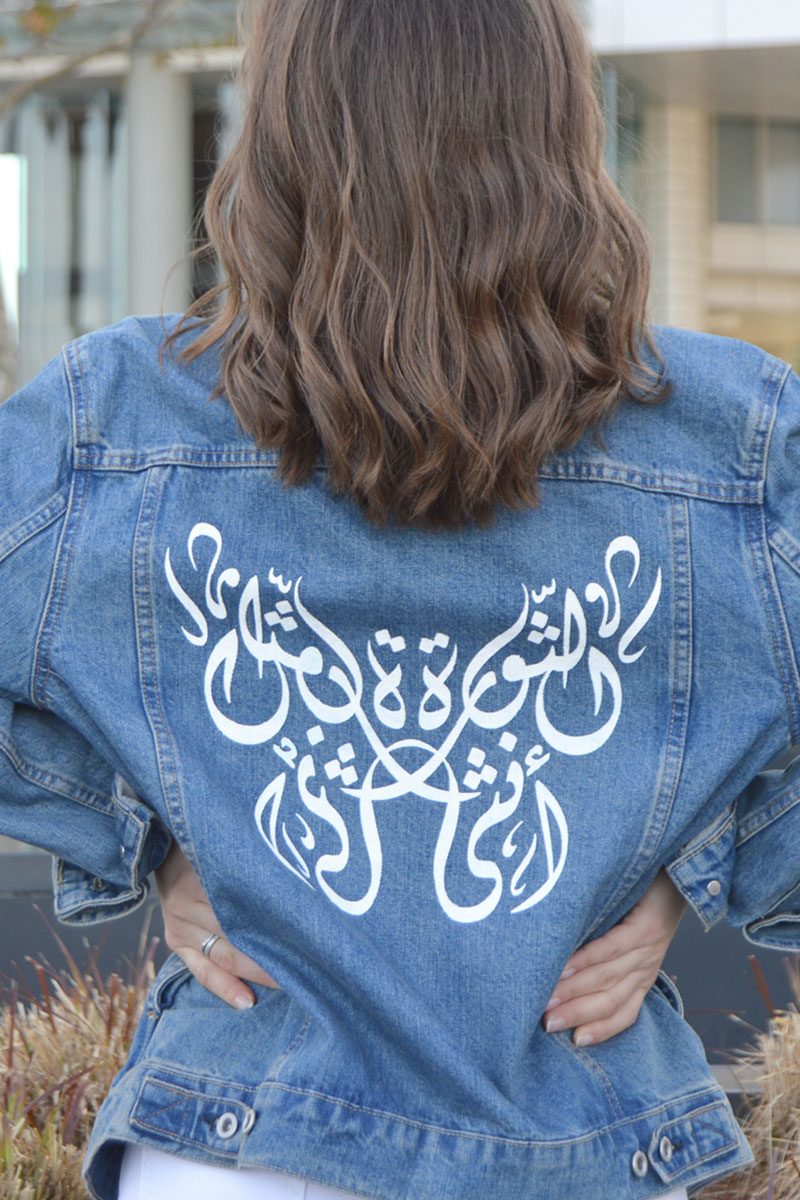 The revolution is Women sentence in Arabic calligraphy hand-painted on a blue denim jacket